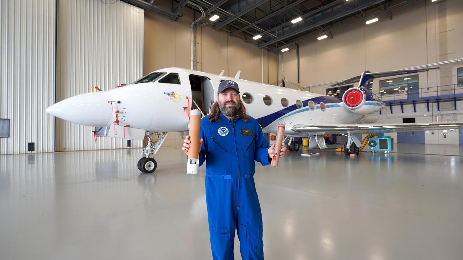 An engineer in a flight suit holds up two weather probes called dropsondes