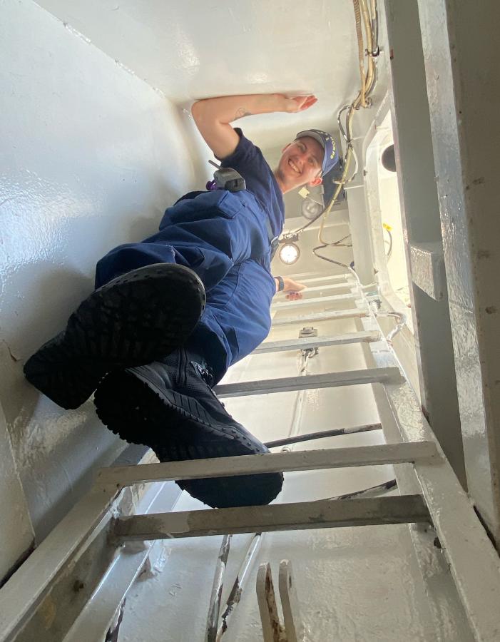 ENS Kyanna Cadwallader looking down from a ladder on a ship.