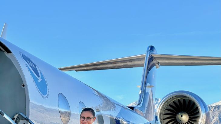 A NOAA Corps officer in a blue flightsuit standing on the stairs to a NOAA jet