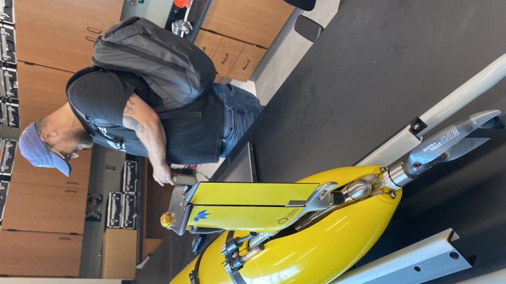 A NOAA employee stands next to a yellow glider on a lab bench.