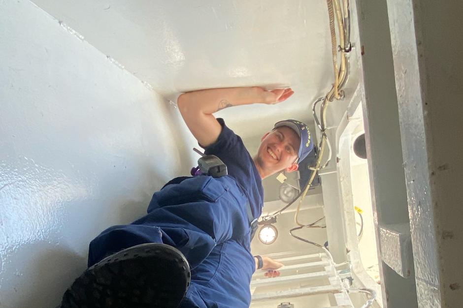 ENS Kyanna Cadwallader looking down from a ladder on a ship.