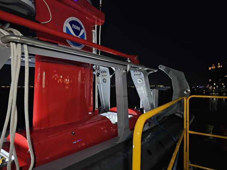 The red DriX uncrewed marine system sits in its gray gondola at night