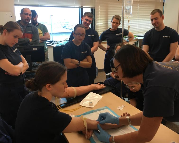 People watching a medical professional insert an I.V. into someone's arm. 