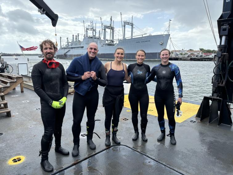 5 people standing on the deck of a ship after diving.